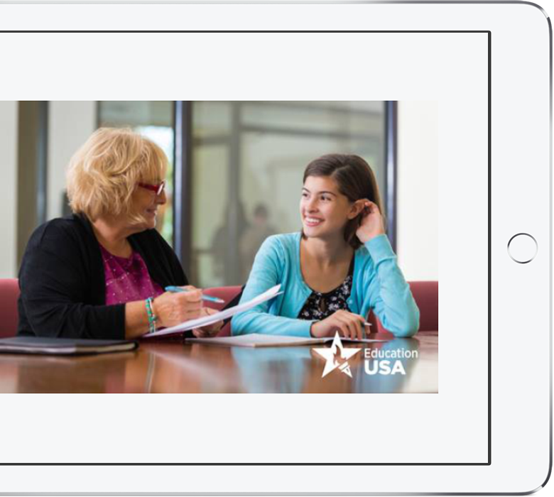 A photo of a young woman and an older woman smiling at each other while signing papers. Education USA watermark visible.